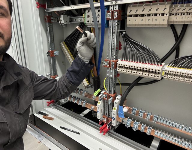 Elektriker verlegt eine Ader an der Sammelschiene eines Schaltschranks